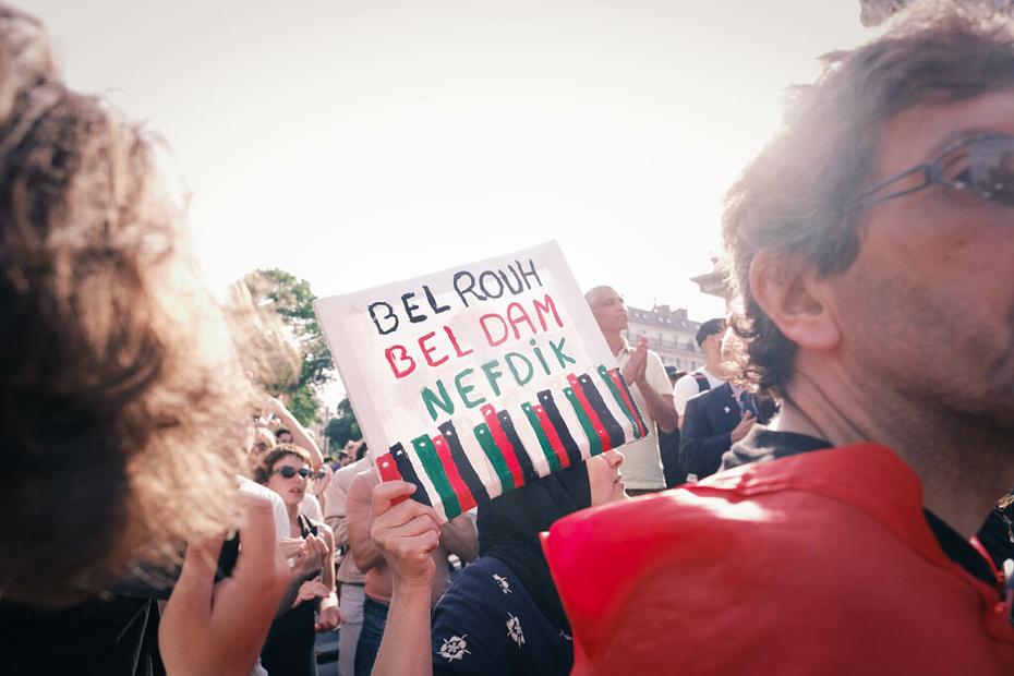 Femme brandissant une pancarte au milieu de la foule. Dessus, inscrit : "Avec notre âme et notre sang, nous te défendons".